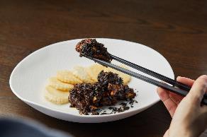 A person holding a pair of chopsticks to a plate of food

Description automatically generated