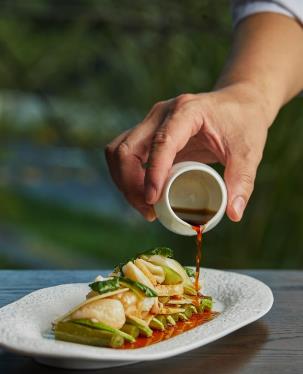 A person pouring sauce on a plate

Description automatically generated